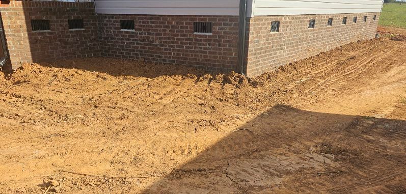 Brick building on a dirt lot with sloped, freshly graded earth around the foundation.