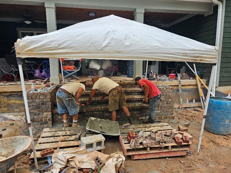 Workers building a brick wall under a white canopy at a construction site