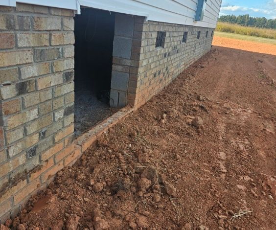 Brick house foundation beside a muddy dirt yard with a doorway and small windows along the wall