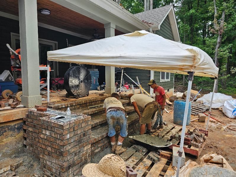 Workers laying brick around a covered patio construction site next to a house