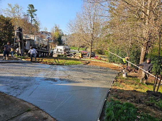 Workers pour fresh concrete on a driveway in a tree-lined residential area.