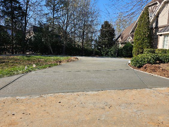 Concrete driveway curving through a landscaped yard with trees and a house in the background