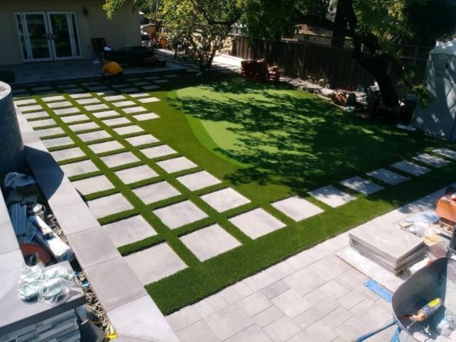 Backyard with square stepping stones in a green lawn beside a patio and house