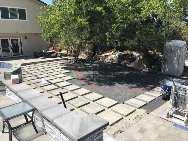 Backyard patio renovation with pavers, sand, and construction tools beside a house