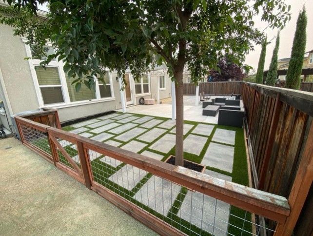 Backyard patio with gray pavers, wooden fence, and outdoor seating beside a house