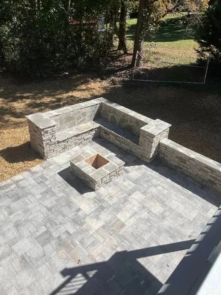 Stone patio with built-in bench seating and a fire pit in a backyard.