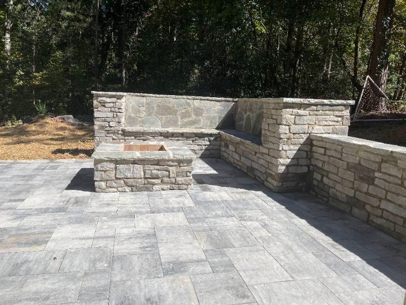 Stone patio with built-in benches and a low wall in a wooded outdoor area