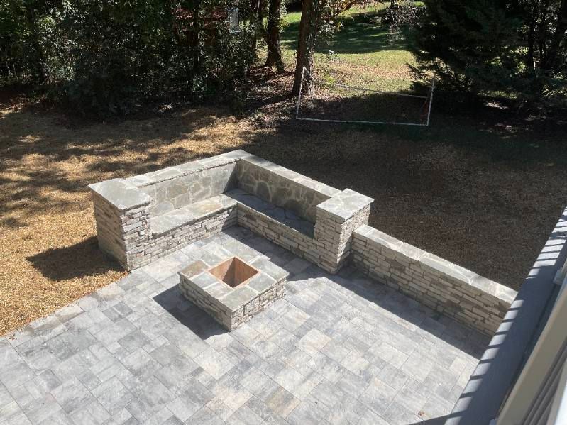 Stone patio with built-in L-shaped seating around a small fire pit in a backyard garden
