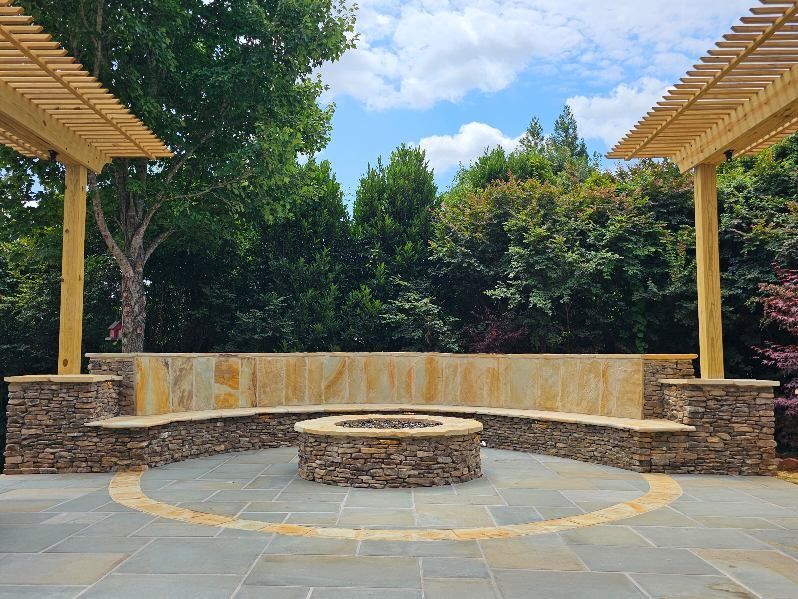 Outdoor stone amphitheater with circular seating, central fire pit, and trees under a partly cloudy sky