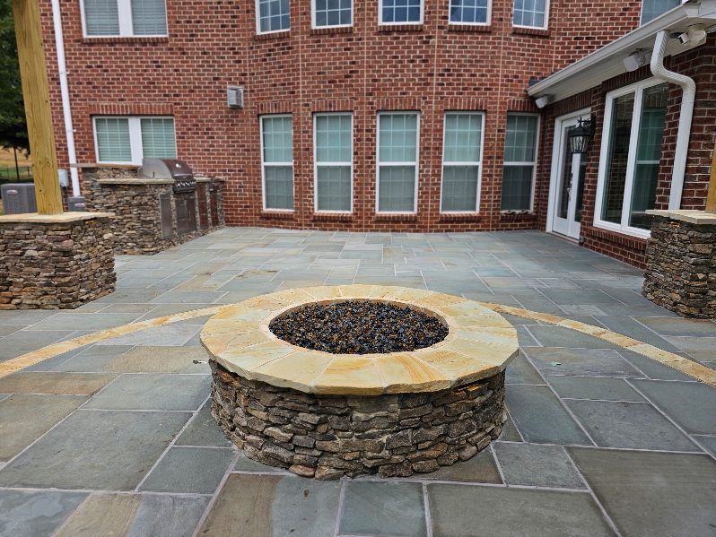 Stone fire pit in a brick courtyard with gray pavers and surrounding stone planters.