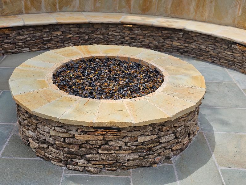 Stone fire pit with circular beige cap and dark rocks in an outdoor courtyard