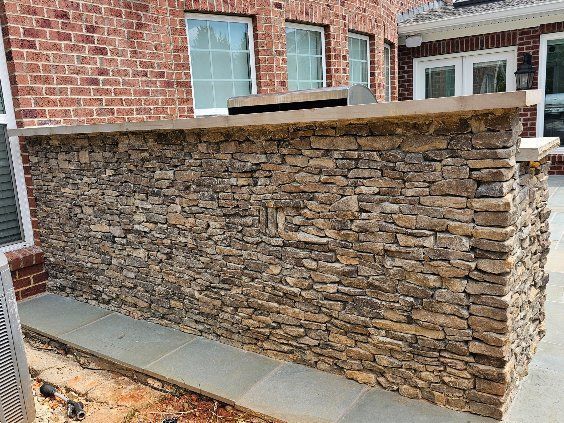 Stone privacy wall beside a brick house with concrete cap and walkway