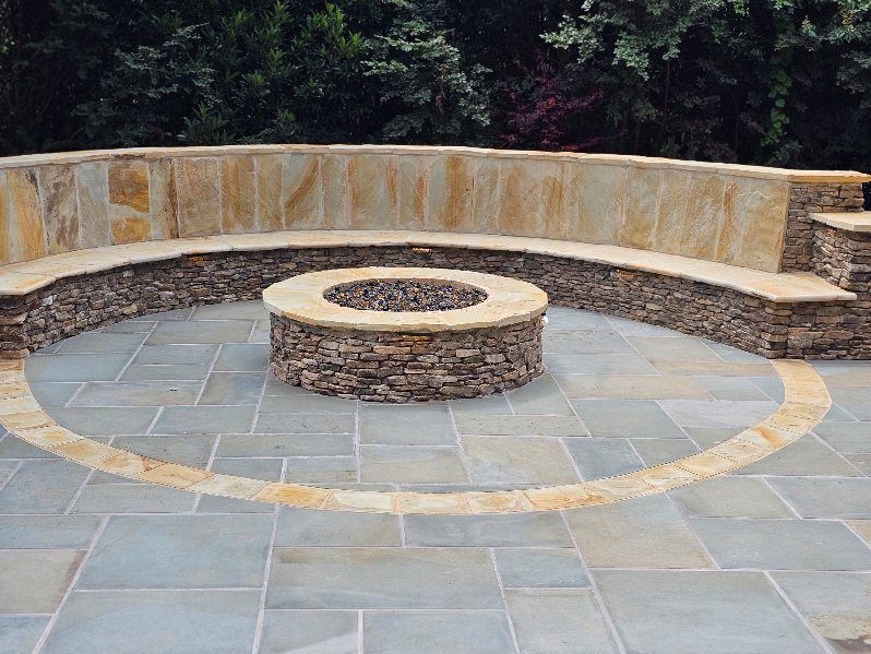 Circular stone fire pit with curved bench seating in an outdoor patio surrounded by trees