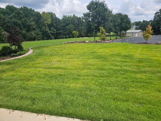 Grassy park with a winding path, trees, and a cloudy sky