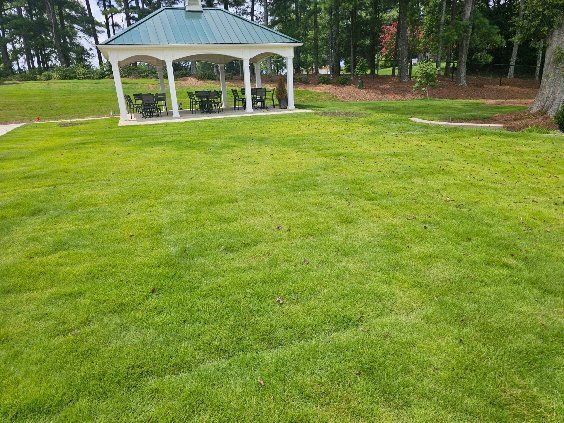 Lush green lawn with a white gazebo and trees in the background