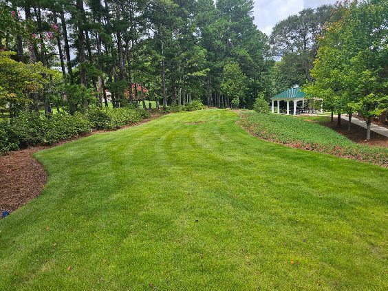 Lush green lawn bordered by trees and shrubs, with a small pavilion in the distance