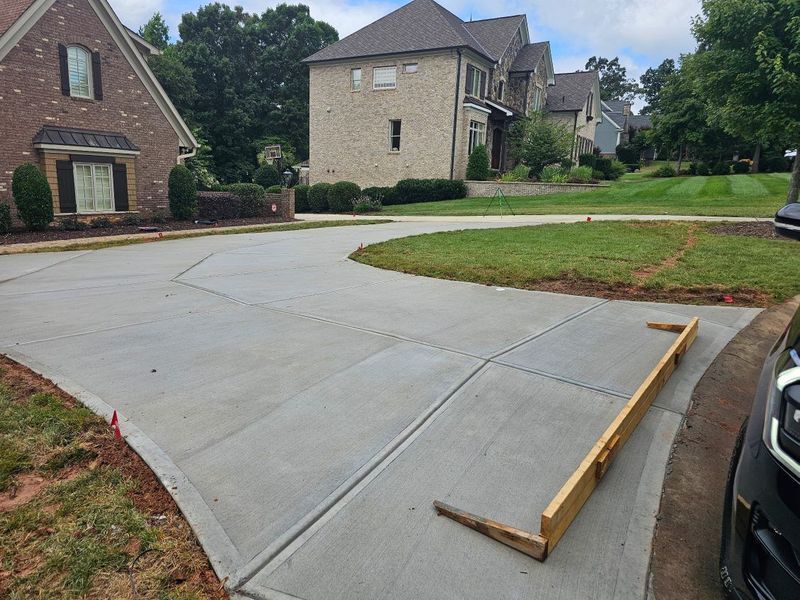 Fresh concrete driveway beside a suburban house, with a wooden form board on the edge