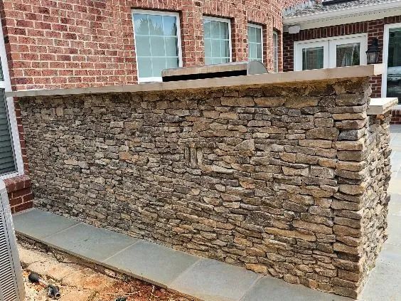 Stone veneer wall beside a brick house with a concrete cap and sidewalk in front