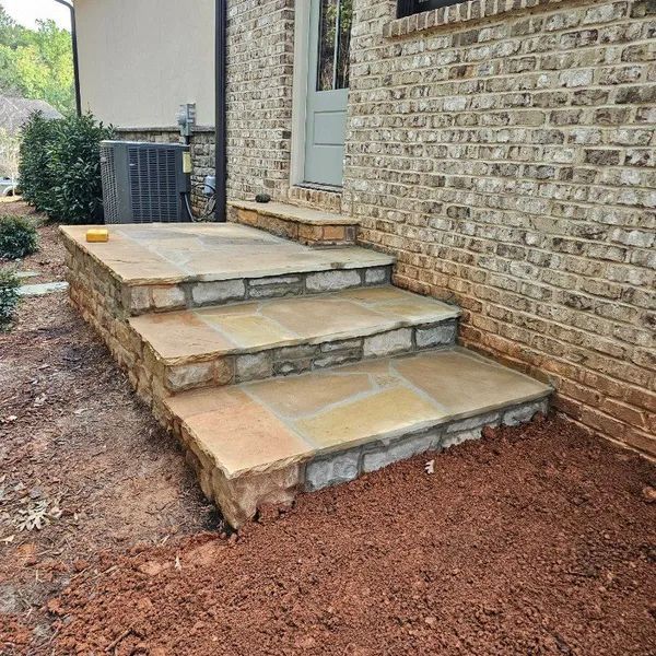 Stone steps beside a brick house leading to a back door, with red gravel landscaping around them