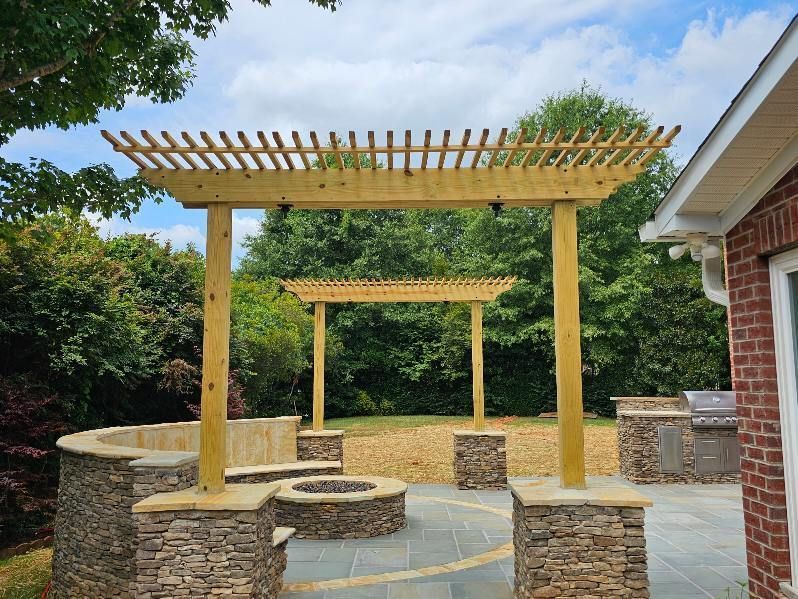 Backyard patio with wooden pergolas, stone seating walls, and a brick house exterior under a blue sky