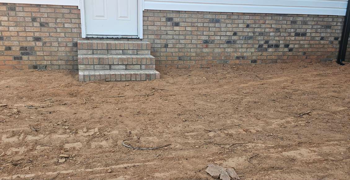 White door with brick steps above a bare dirt yard in front of a brick house