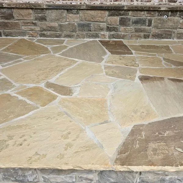 Stone patio with irregular tan and brown flagstones beside a stacked stone wall.