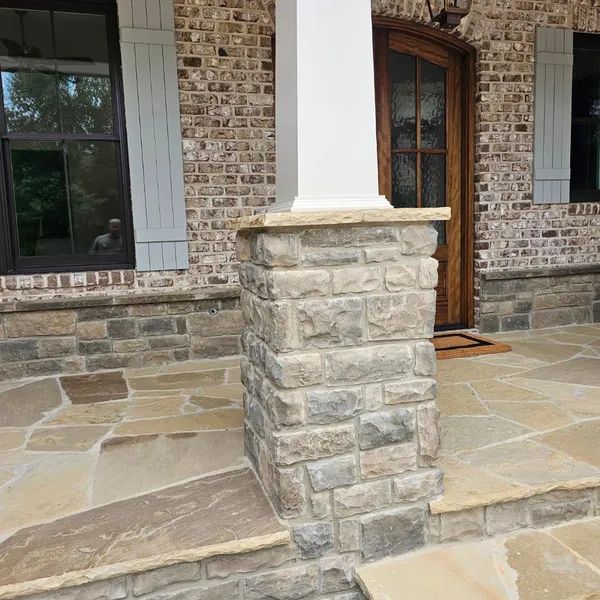Stone porch column beside a wooden front door on a brick house with a flagstone patio
