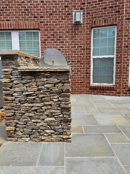 Stone outdoor grill beside a brick house on a paved patio