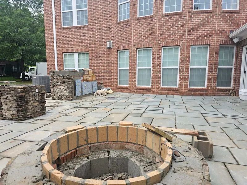 Backyard patio with a circular stone fire pit in front of a brick house.