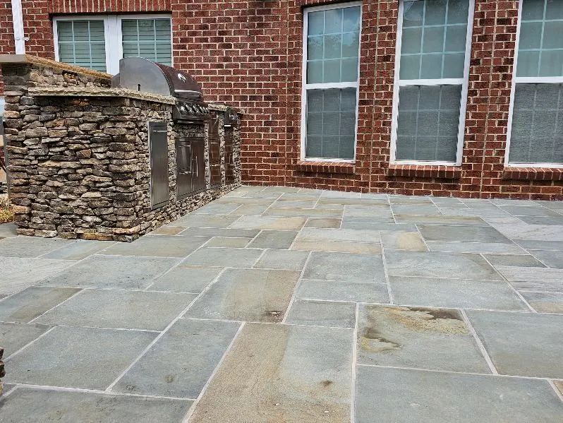Stone patio beside a red brick house with large windows and a low stacked-stone wall