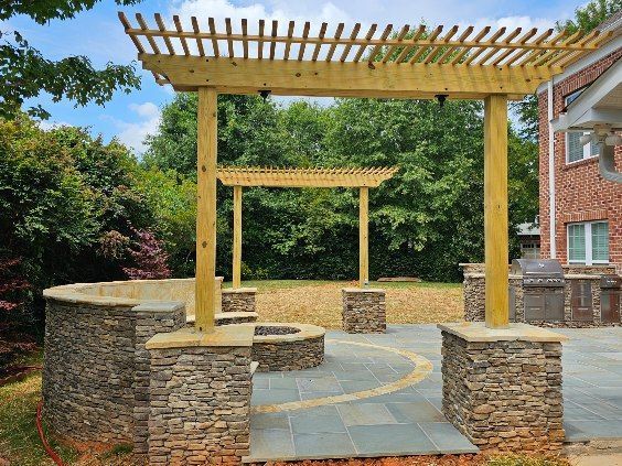 Stone patio with wooden pergola and curved seating wall in a landscaped garden