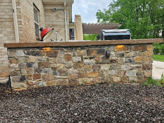 Stone garden wall with a black metal fence, gravel foreground, and a small red object near a house.