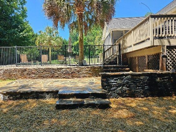 Stone steps leading to a wooden deck and fenced backyard with trees and dry ground
