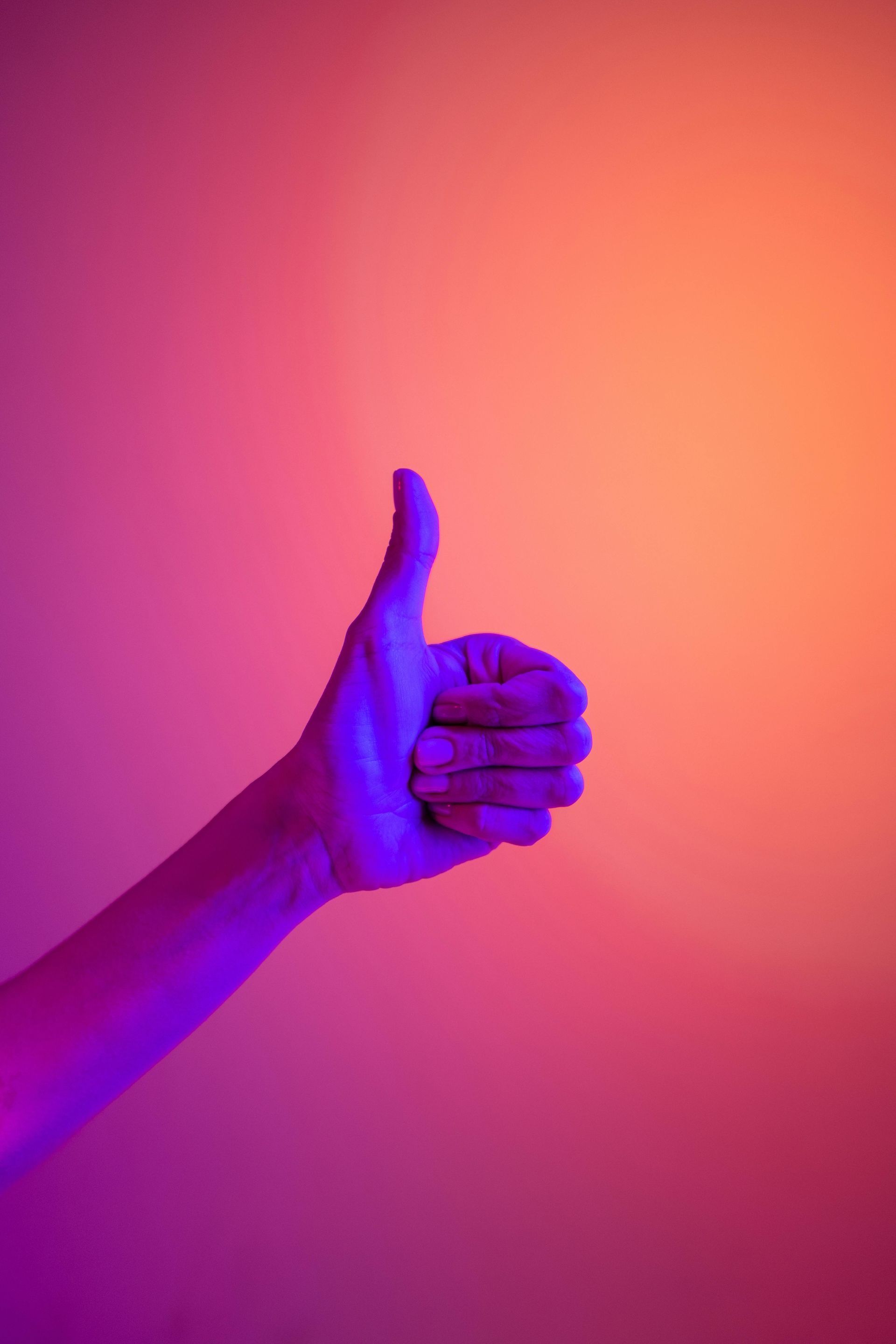 A hand is giving a thumbs up sign in front of a purple and orange background.