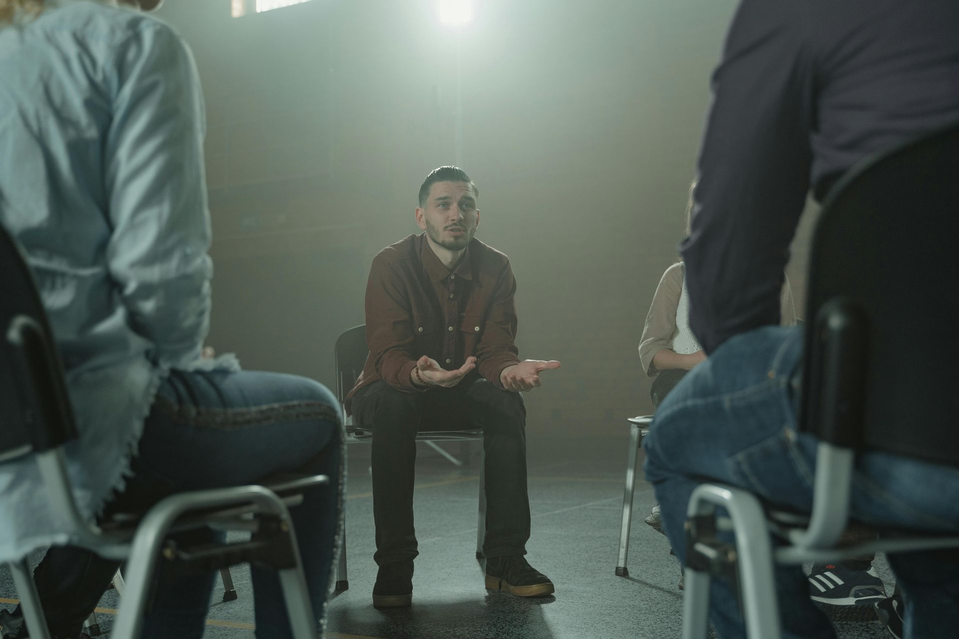 Man speaking in a group, gesturing; seated in circle with others.