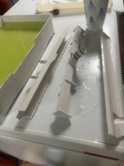 White plastic darkroom equipment, including trays and a part with a nozzle, on a white surface with green liquid.
