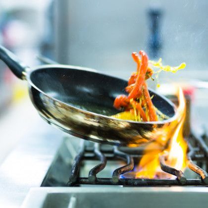 A frying pan on fire above a gas stove, with food and flames.
