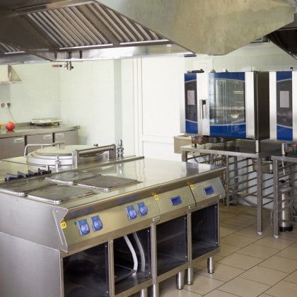 Commercial kitchen with stainless steel appliances, vent hood, and ovens.