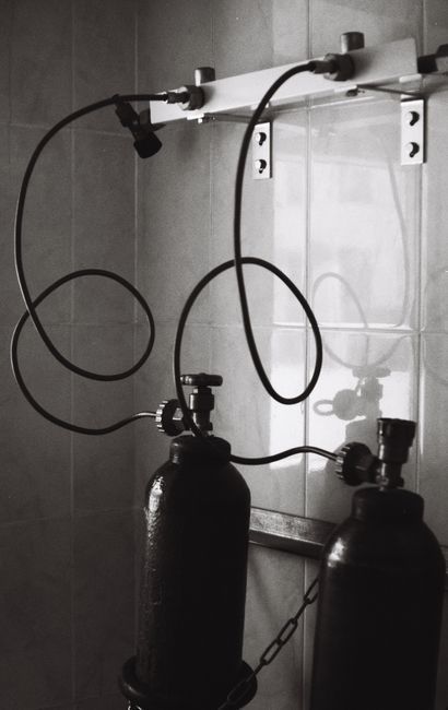 Dos bombonas de gas negro con mangueras enrolladas montadas en una pared de una habitación alicatada.