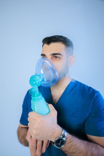 Hombre usando una mascarilla nebulizadora azul, sosteniendo el dispositivo contra su rostro sobre un fondo azul claro liso.