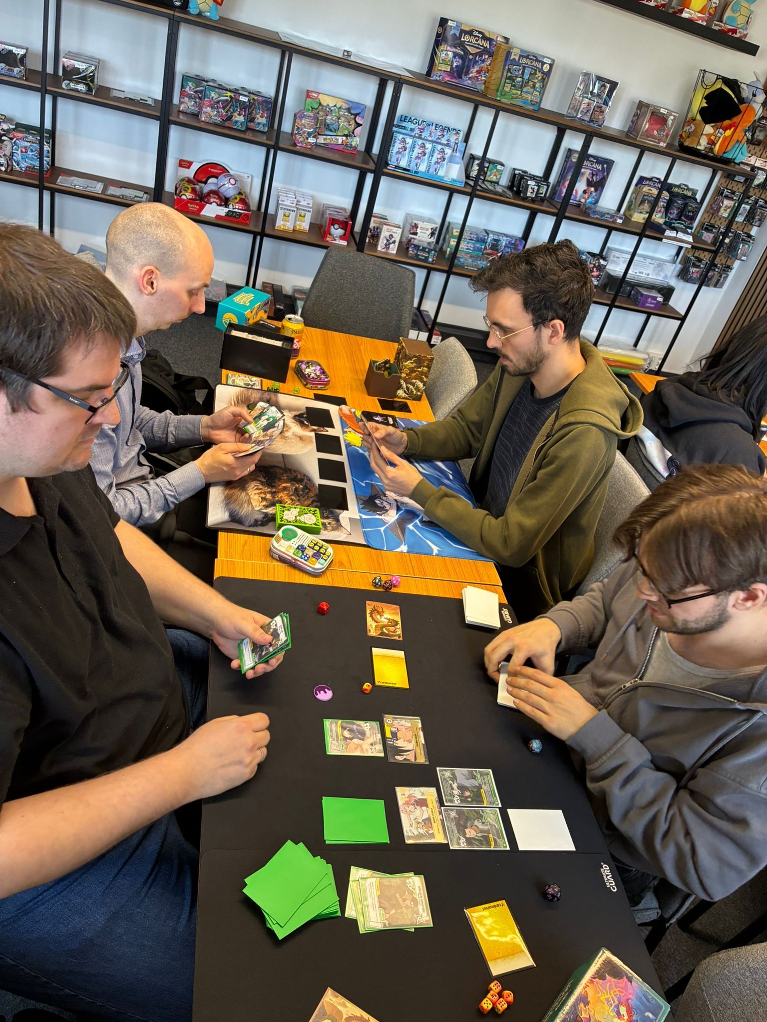 People playing a colorful card game at a long table in a room with shelves of games.