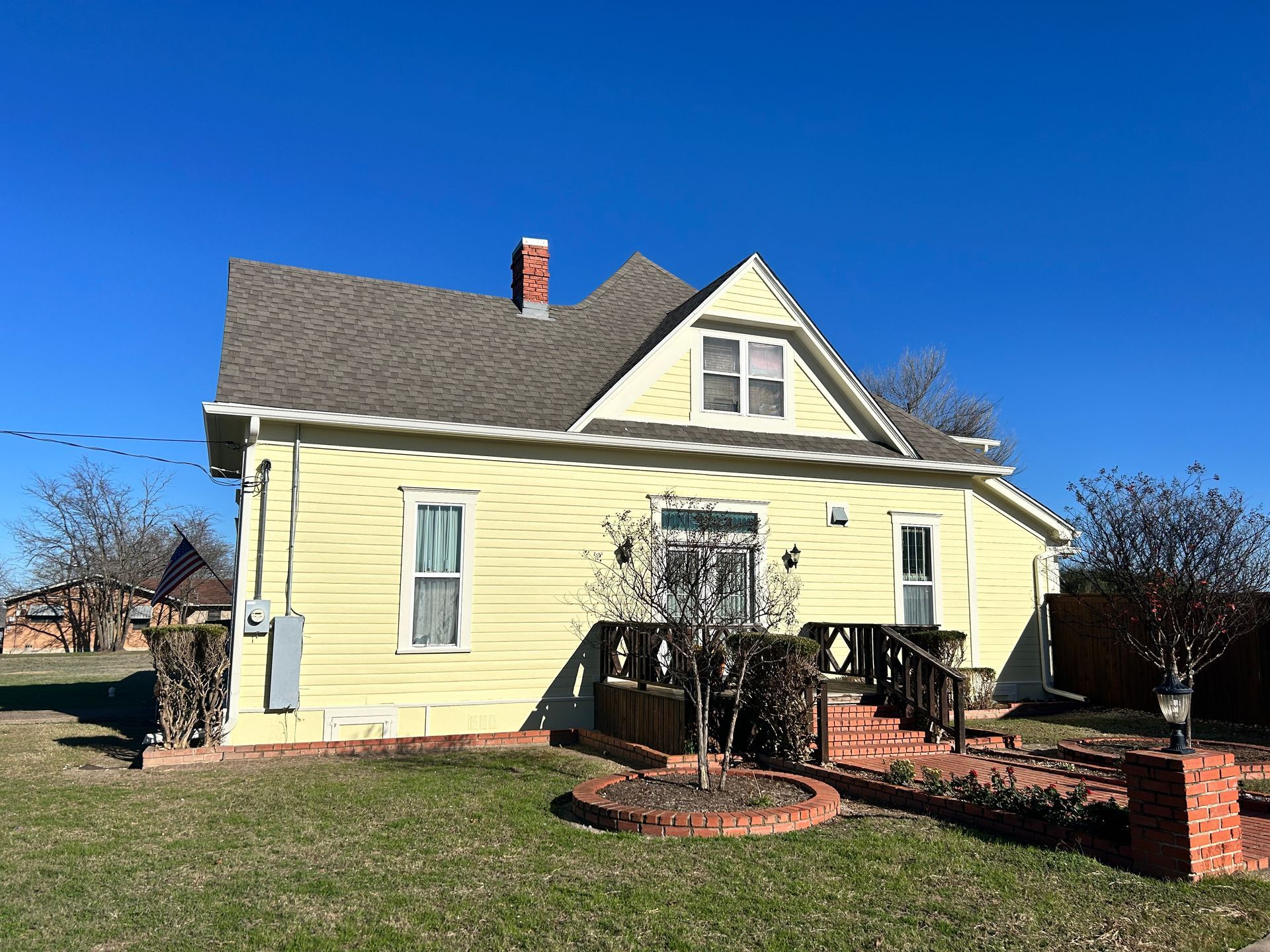 Yellow house with gabled roof, brick porch, and clear blue sky.