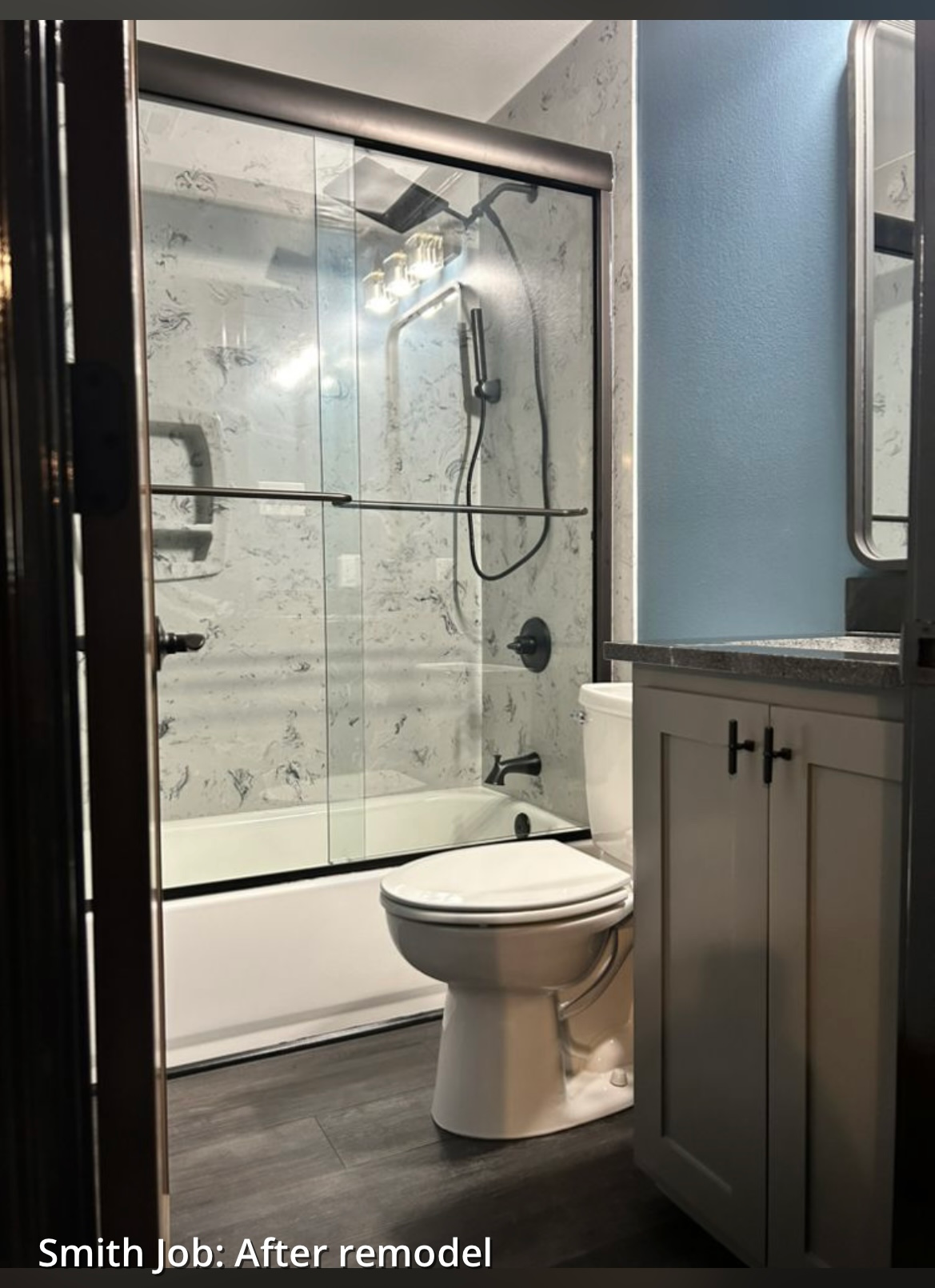 Bathroom remodel: Gray marbled shower, light blue wall, white vanity, toilet, and gray flooring.