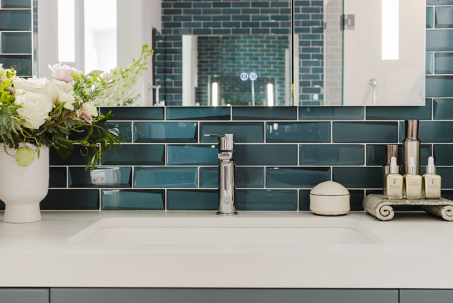 A bathroom sink with blue tiles and a vase of flowers on the counter.