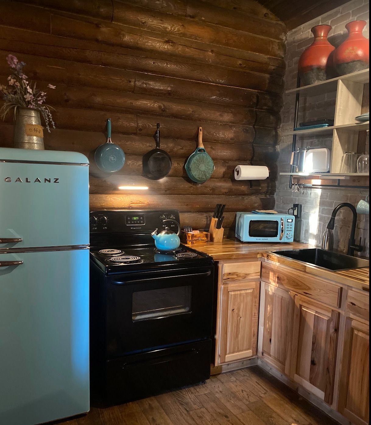 A kitchen with a blue refrigerator , stove , sink and microwave.