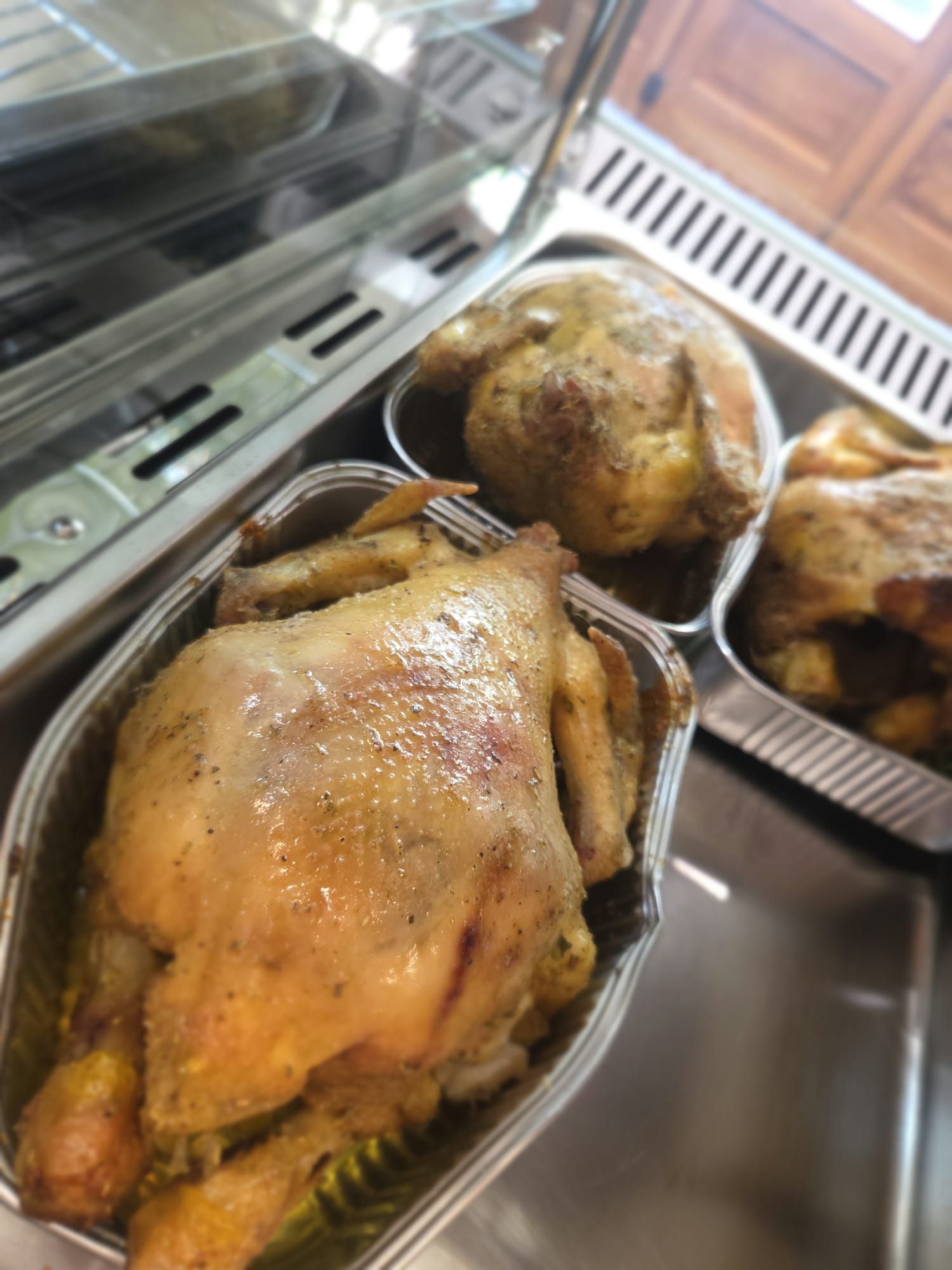 Polli arrostiti in vassoi di alluminio all'interno di una vetrina da gastronomia