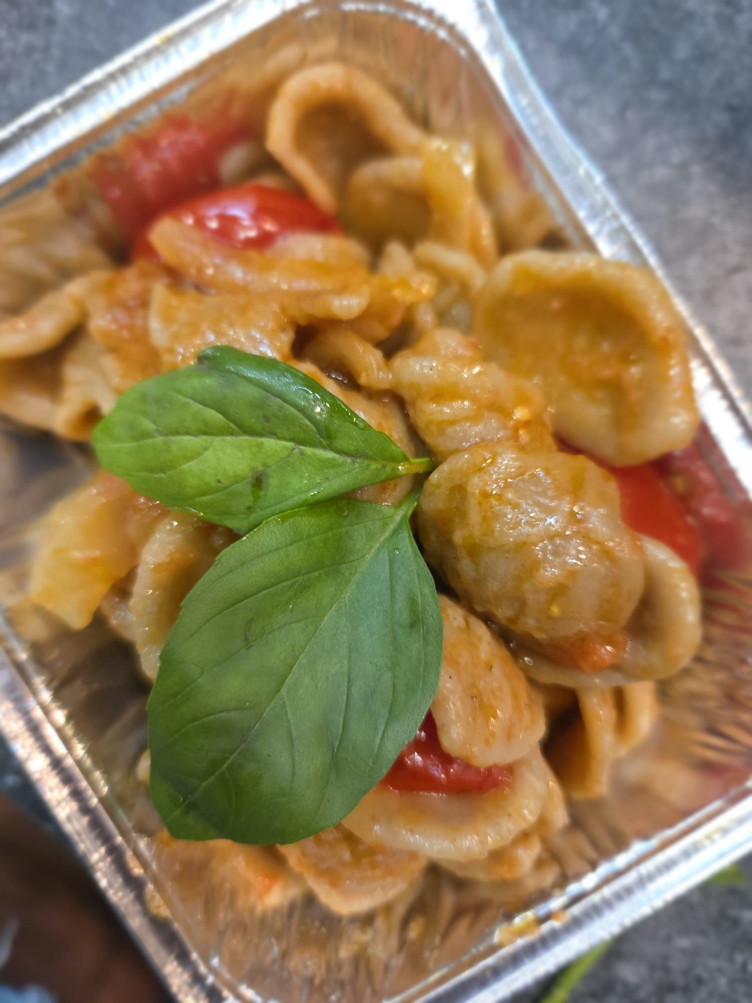 Vassoio di pasta con pollo e salsa di pomodoro, guarnita con foglie di basilico fresco.