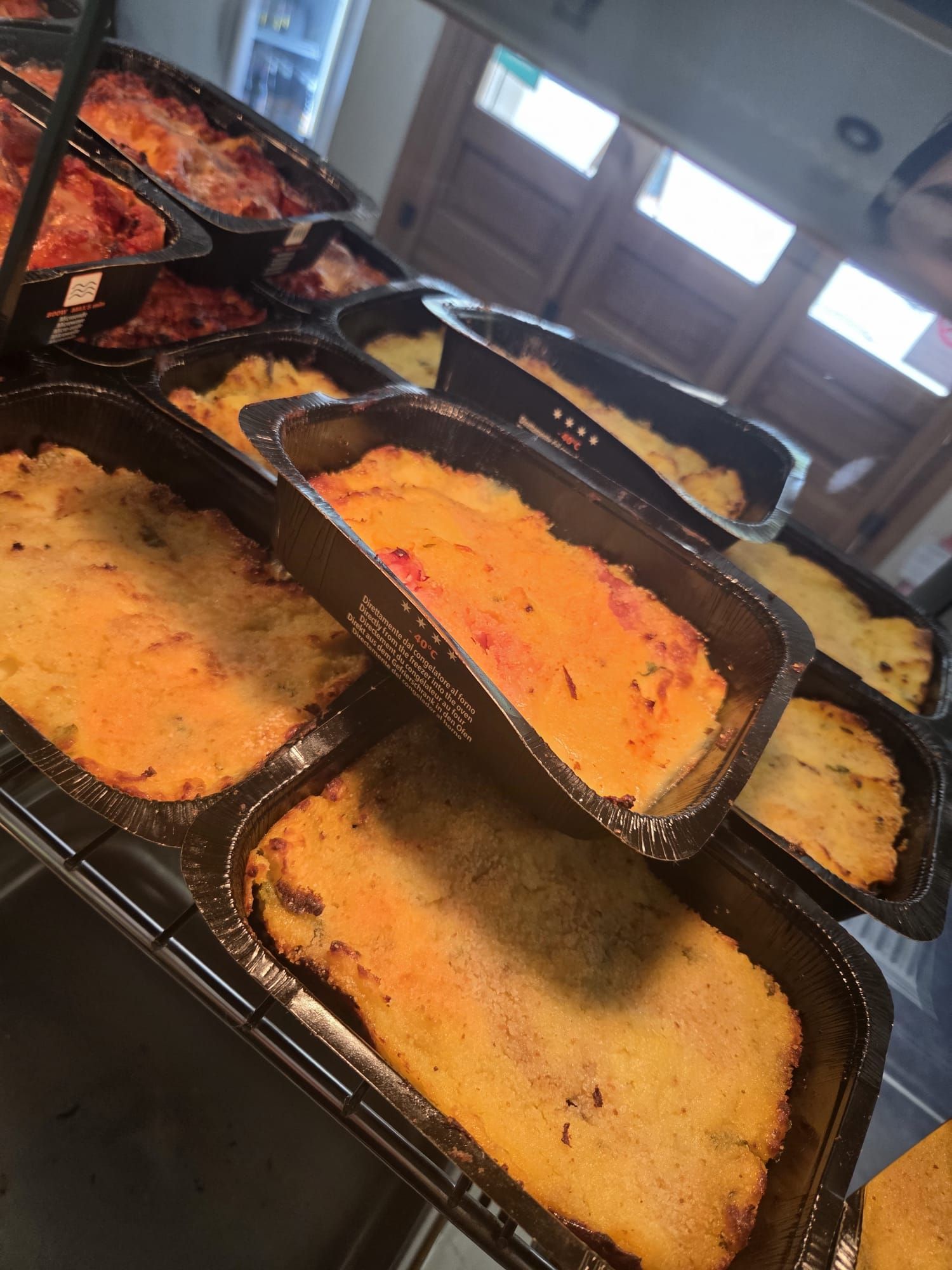 Vassoi neri di sformati al forno disposti su una linea da buffet, con superfici arancioni e dorate sotto una calda luce interna.