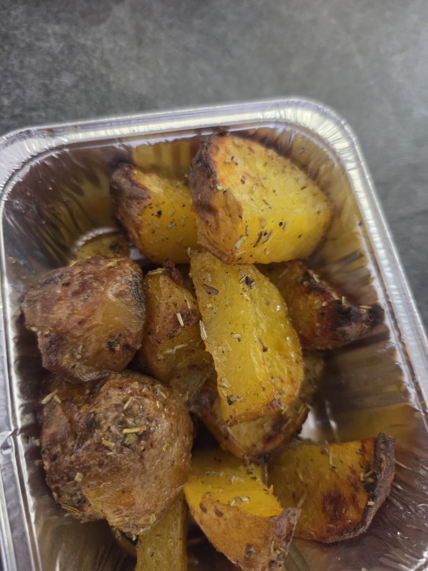 Contenitore in alluminio di spicchi di patate arrosto con condimento dorato