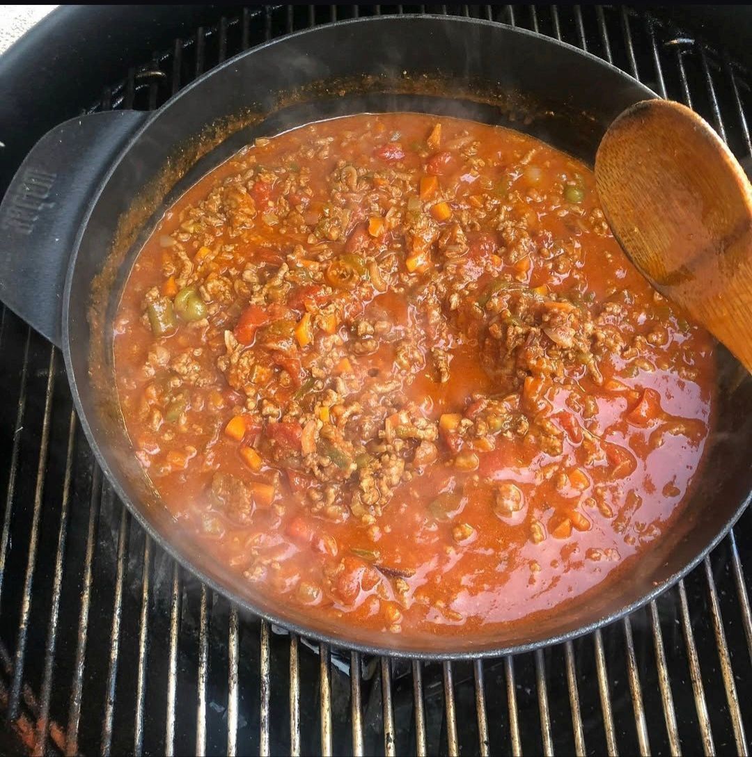 Una padella di ragù di carne rossa che sobbolle su una griglia, con un cucchiaio di legno appoggiato sul bordo.
